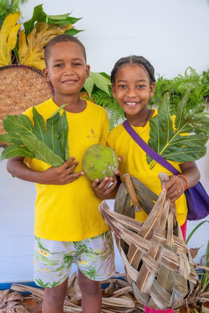 Children displaying breadfruit, leaves and traditional woven crafts